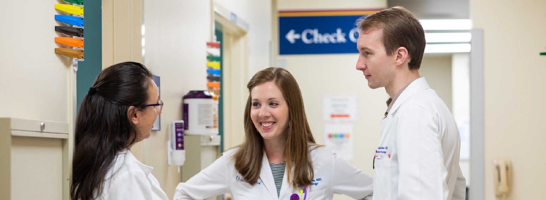 Two female and one male physician talk in hallway.